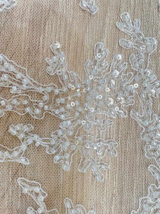 Detalle de mostacilla perlada y lentejuelas transparentes sobre tul blanco para novias