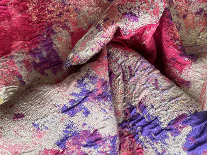 Tela jacquard metalizada dorada con estampado floral fucsia y morado, primer plano de textura brocada