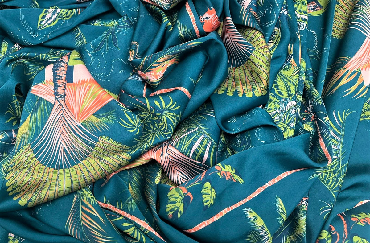 Seda francesa petróleo con estampado tropical de palmas verde limón y coral, drapeada, mostrando su brillo