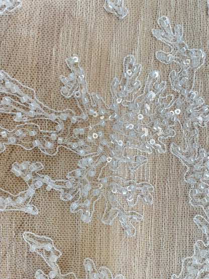 Detalle de mostacilla perlada y lentejuelas transparentes sobre tul blanco para novias