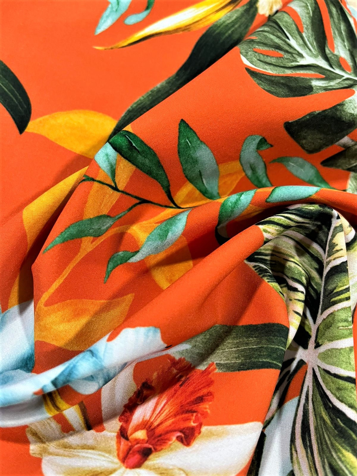Seda francesa naranja con orquídeas y hojas tropicales drapeada, mostrando su brillo y caída fluida