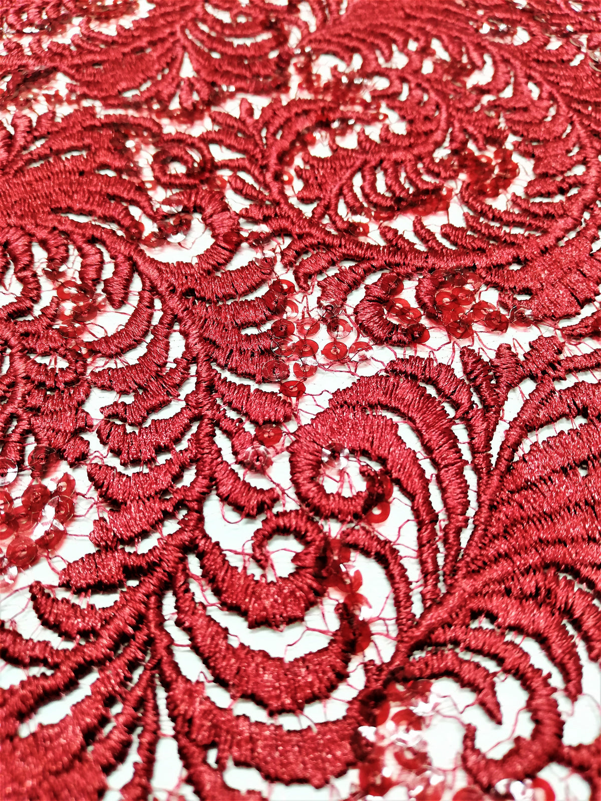 Detalle de encaje rojo con plumas en relieve y lentejuelas rojas y transparentes