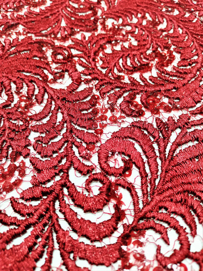 Detalle de encaje rojo con plumas en relieve y lentejuelas rojas y transparentes